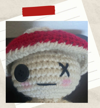 embroidered face details on a crochet toadstool doll including an X and a button eye