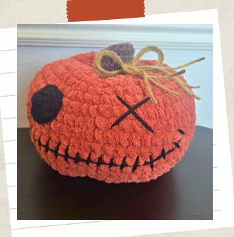 Finished crochet pumpkin amigurumi with whimsical stitched face and pumpkin stem