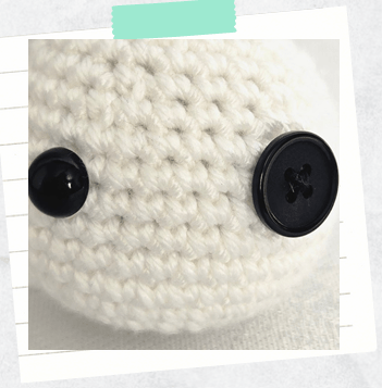 a close up showing placement of safety eye and button for amigurumi snowman patterns.