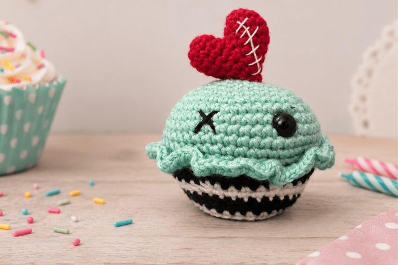 A finished whimsical crochet cupcake in front of a festive birthday background.