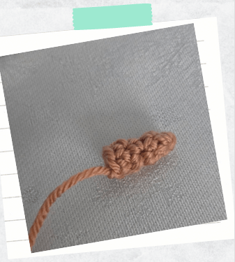 A tutorial photo showing a crocheted carrot nose for a crochet snowman amigurumi.
