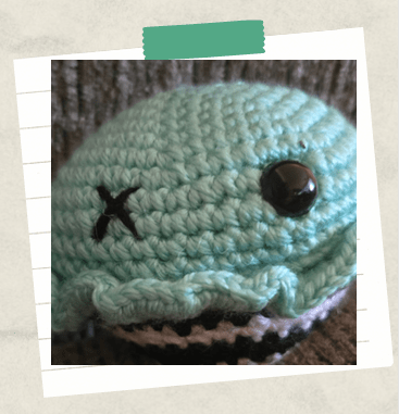 A tutorial image showing an embroidered X to create an eye on a crochet cupcake.